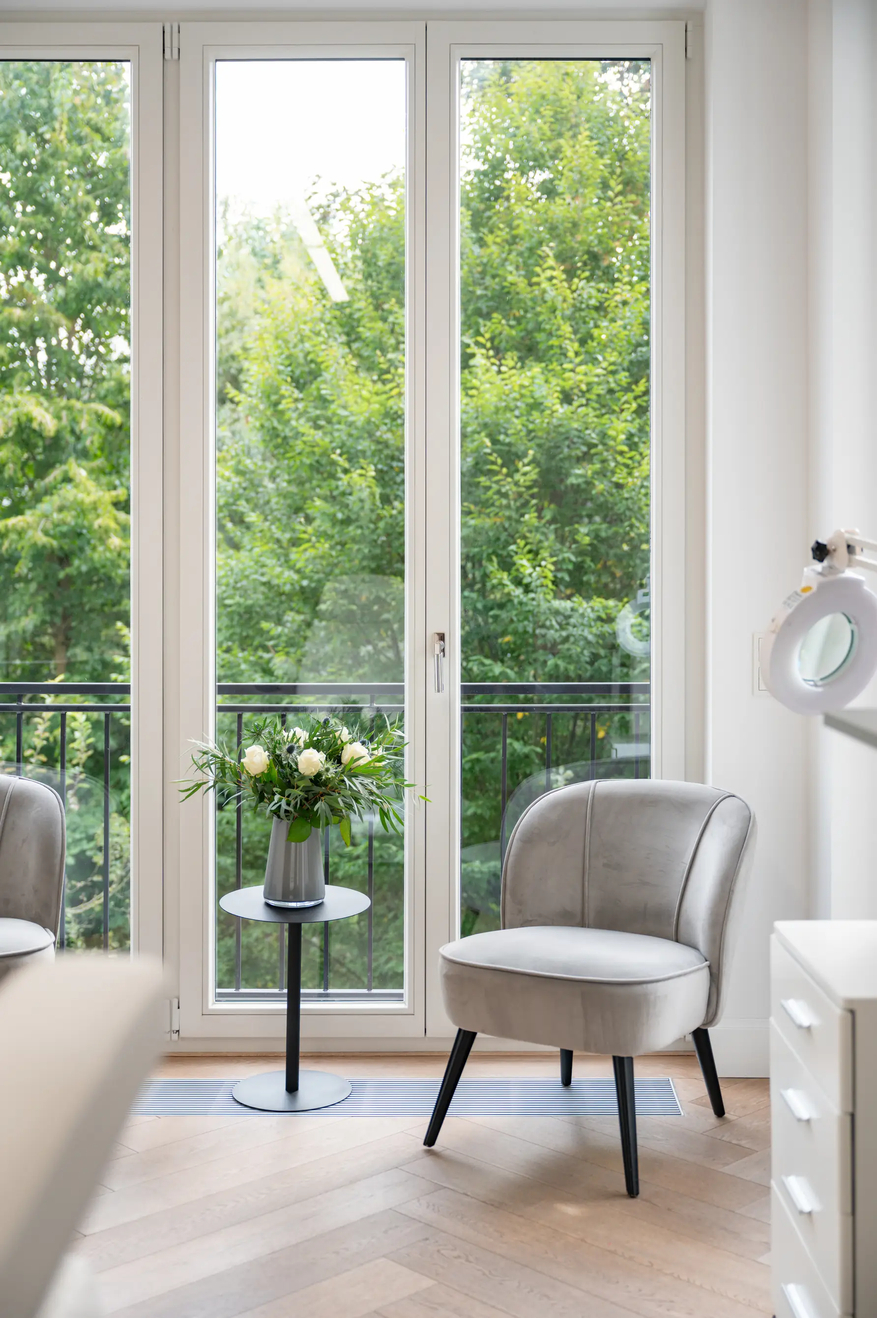 Beratungsraum von innen:
Modernes Zimmer mit grauem Sessel, kleinem Tisch mit Blumen und großen Fenstern mit Blick auf grüne Bäume.