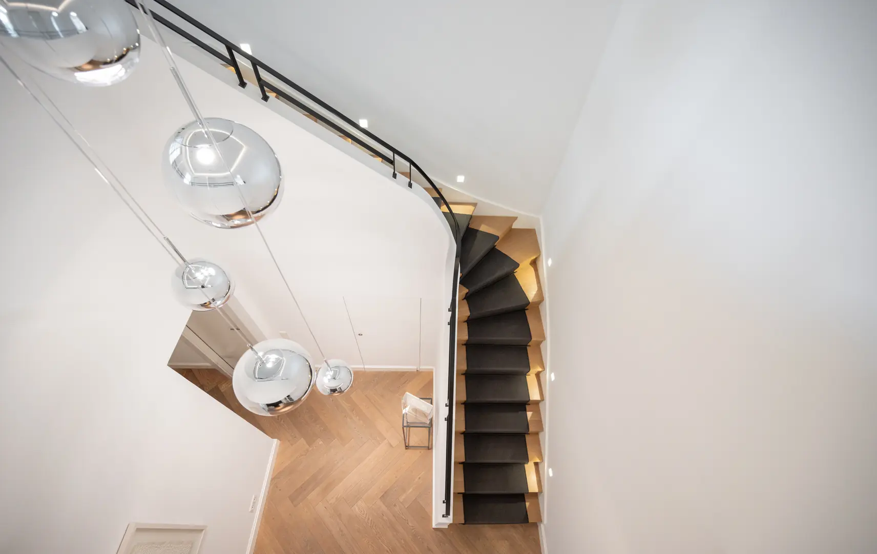 Moderne Holztreppe mit schwarzem Teppich und hängenden silbernen Kugelleuchten in weißem Raum.